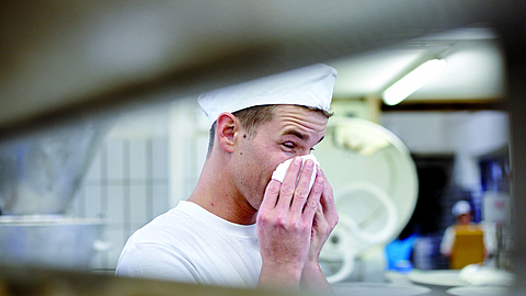 Junger Bäcker ist erkältet und putzt sich die Nase mit einem Taschentuch