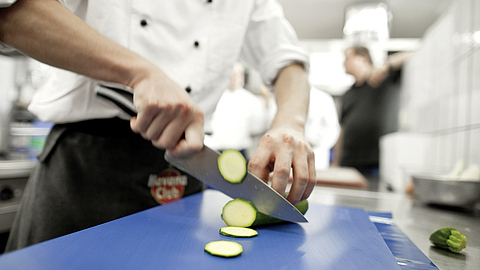 Koch schneidet mit einem großen Messer eine Gurke in Scheiben