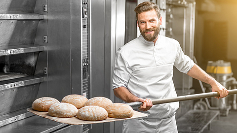 Bäcker holt fertig gebackenes Brot aus dem Ofen