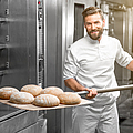 Bäcker holt fertig gebackenes Brot aus dem Ofen