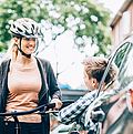 Eine Fahrradfahrerin unterhält sich mit einem Autofahrer durch das offene Fenster auf einer Straße.