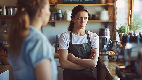 Servicekraft eines Kaffees verschränkt die Arme und blickt wütend zur Seite