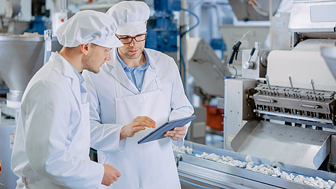 Zwei junge männliche Sicherheitsbeauftragte  kontrollieren die automatisierte Produktion in der Nahrungsmittelindustrie