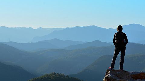 Eine Person steht auf einem Berggipfel und schaut in die Ferne.