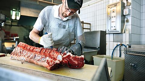 Fleischer bei Zerlegearbeiten mit Stechschutz und Schnittschutzhandschuh an Messer führender Hand