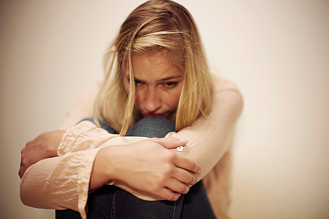 Eine Frau sitzt mit verschränkten Armen und traurigem Gesicht an einer Wand.