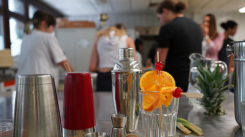 Mit Obst dekoriertes Cocktailglas umgeben von Barmixgeräten.