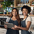 Zwei Frauen arbeiten im Bistro hinterm Tresen und schauen auf ein Tablet.