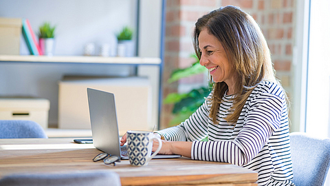 Glückliche Frau arbeitet am Laptop von zu Hause