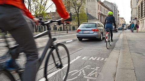 Blick in eine Straße mit zwei Fahrradfahrern und einem Auto von hinten.