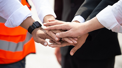 Fünf Personen stehen im Kreis und legen jeweils die rechte Hand übereinander