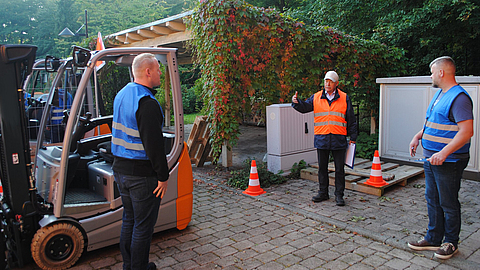 Dozent erklärt zwei Seminarteilnehmern etwas im Innenhof der Bildungsstätte Reinhardsbrunn neben einem Flurförderzeug