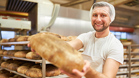 Auch für das Backgewerbe gilt: Die demografischen Veränderungen und der steigende technologische Fortschritt erfordern langfristige und nachhaltige Lösungen, um dem Fachkräftewandel entgegenzuwirken. | © Robert Kneschke - stock.adobe.com Junger Bäcker zeigt ein frisches und gesundes Biobrot