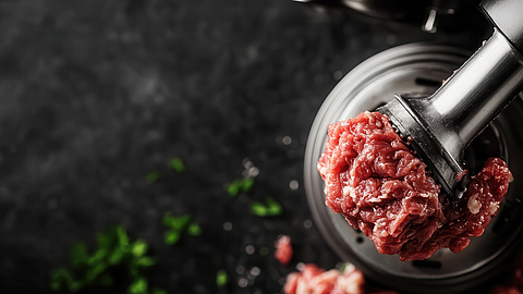 Frisch gehacktes Fleisch, das durch einen Fleischwolf verarbeitet wird mit verstreuten Stücken und Kräutern