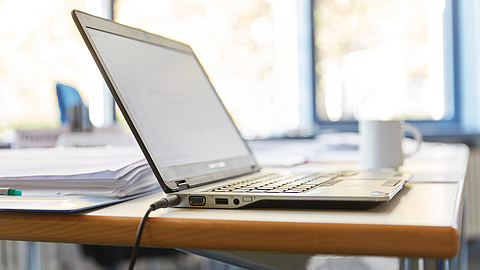 Ein Laptop steht auf einem Tisch, im Hintergrund eine Tasse.
