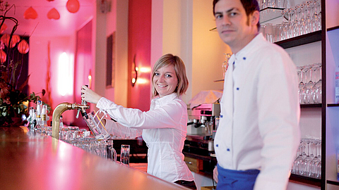 Servicekraft zapft ein Bier, daneben ein Koch