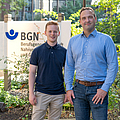 Von links: Jonas Brenneis und Dr. Andre Becker stehen lächelnd vor einem Schild der Berufsgenossenschaft Nahrungsmittel und Gastgewerbe (BGN) | © BGN/Saskia Nagel Von links: Jonas Brenneis und Dr. Andre Becker stehen lächelnd vor einem Schild der Berufsgenossenschaft Nahrungsmittel und Gastgewerbe (BGN)