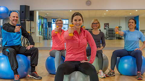 Gruppe trainiert mit Hanteln auf dem Gymnastikball