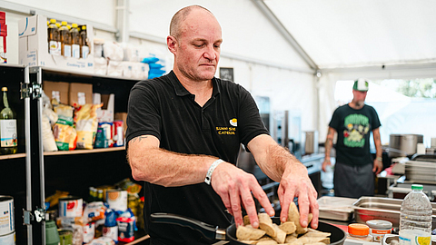 John Cusack, Koch bei Sunny Side Catering, brät Würstchen für die Künstler des Highfield-Festivals.