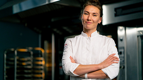 Porträt einer Bäckerin in Uniform in einer Bäckerei vor dem Hintergrund eines Ofens und frischer Backwaren