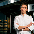 Porträt einer Bäckerin in Uniform in einer Bäckerei vor dem Hintergrund eines Ofens und frischer Backwaren