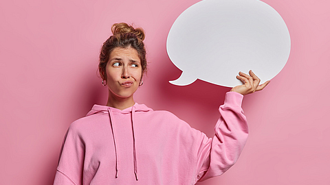 Aufnahme einer nachdenklichen Frau mit Kommunikationsblase  Sweatshirt vor rosa Hintergrund