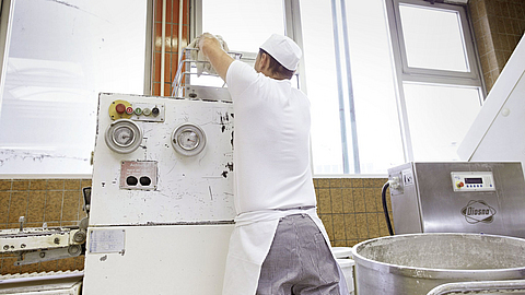 Bäcker wirft über Kopf Teigklumpen in den   Trichter eines Teigteilers                                              Trichter eines Teigteilers