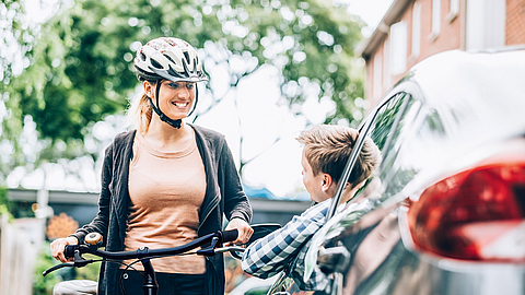 Eine Fahrradfahrerin unterhält sich mit einem Autofahrer durch das offene Fenster auf einer Straße. | © iStock - FOTOGRAFIA INC. Eine Fahrradfahrerin unterhält sich mit einem Autofahrer durch das offene Fenster auf einer Straße.
