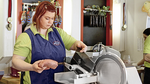 Fleischereifachverkäuferin an der Aufschnittschneidemaschine | © Oliver Rüther/BGN Fleischereifachverkäuferin an der Aufschnittschneidemaschine