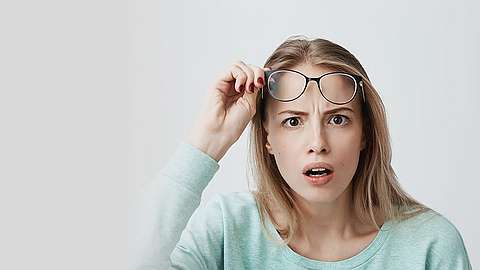 Eine Frau reißt vor Erstaunen die Augen auf und zieht ihre Brille ab.