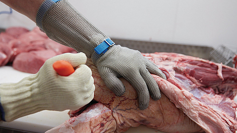 Ausbeinarbeit mit Schnittschutzhandschuh an Messer führender Hand und Stechschutzhandschuh an der anderen Hand