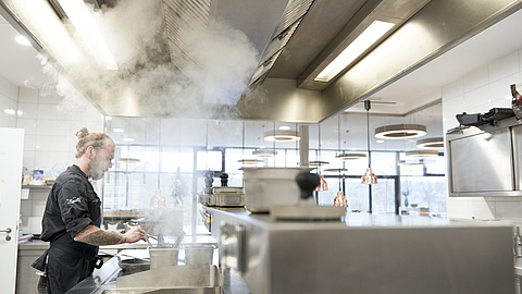 Küchenlüftung: Koch steht am Herd, Wasserdampf zieht aus Topf nach oben