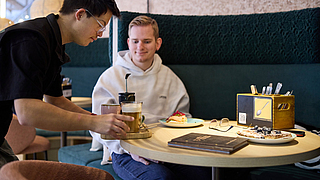 Matheo Schultheis arbeitet seit der Eröffnung im Service – QR-Codes an den Tischen vereinfachen Bestell- und Bezahlvorgänge. | © Dominik Buschardt Matteo Schultheis bedient Gast im Inklusionscafé Coffee, Brownies and Downies