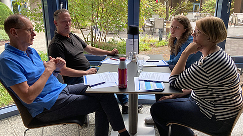 Je nach Größe eines Betriebs empfiehlt sich ein festes Gremium, das die eingegangenen Vorschläge prüft und mitentscheidet, ob und in welcher Form sie umgesetzt und prämiert werden. | © BGN Diskussion in Kleingruppen an einem Tisch