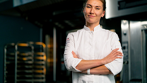 Porträt einer Bäckerin in Uniform in einer Bäckerei vor dem Hintergrund eines Ofens und frischer Backwaren