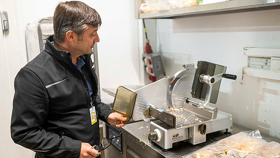 Seinem Blick entgeht so gut wie nichts: Christian Markmann-Lange sieht sofort, dass im Küchenbereich an dieser Aufschnittschneidemaschine die Schlittenrückwand fehlt. | © Martin Hangen München Die BGN auf dem Oktoberfest, Prüfung einer Aufschnittschneidemaschine