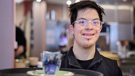 Matheo Schultheis mag besonders den Kundenkontakt: „Ich rede gern mit den Gästen.“ | © Dominik Buschardt Mitarbeiter Matheo Schultheis im Inklusionscafé Coffee, Brownies and Downies