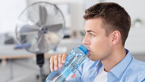 Mann trinkt Wasser im Büro mit Ventilator im Hintergrund