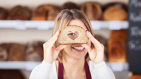 Verkäuferin schaut durch ein Brot mit Herz