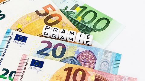 Verschiedene Geldscheine und das Wort Prämie als Buchstabenklötze.