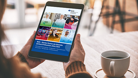 Person schaut auf dem Tablet das Titelbild des BGN-Jahrbuchs Prävention 2024/2025 an